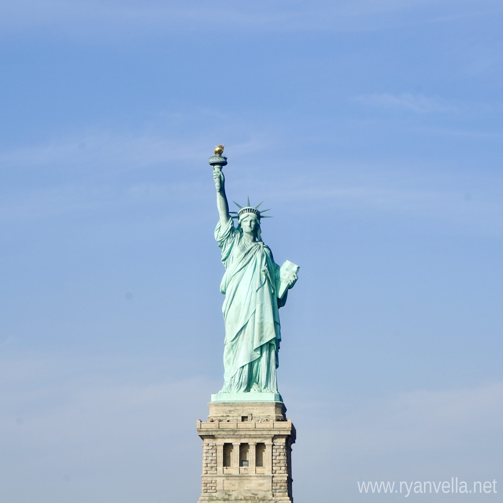 The Statue of Liberty on its stone pedestal against a pale blue sky