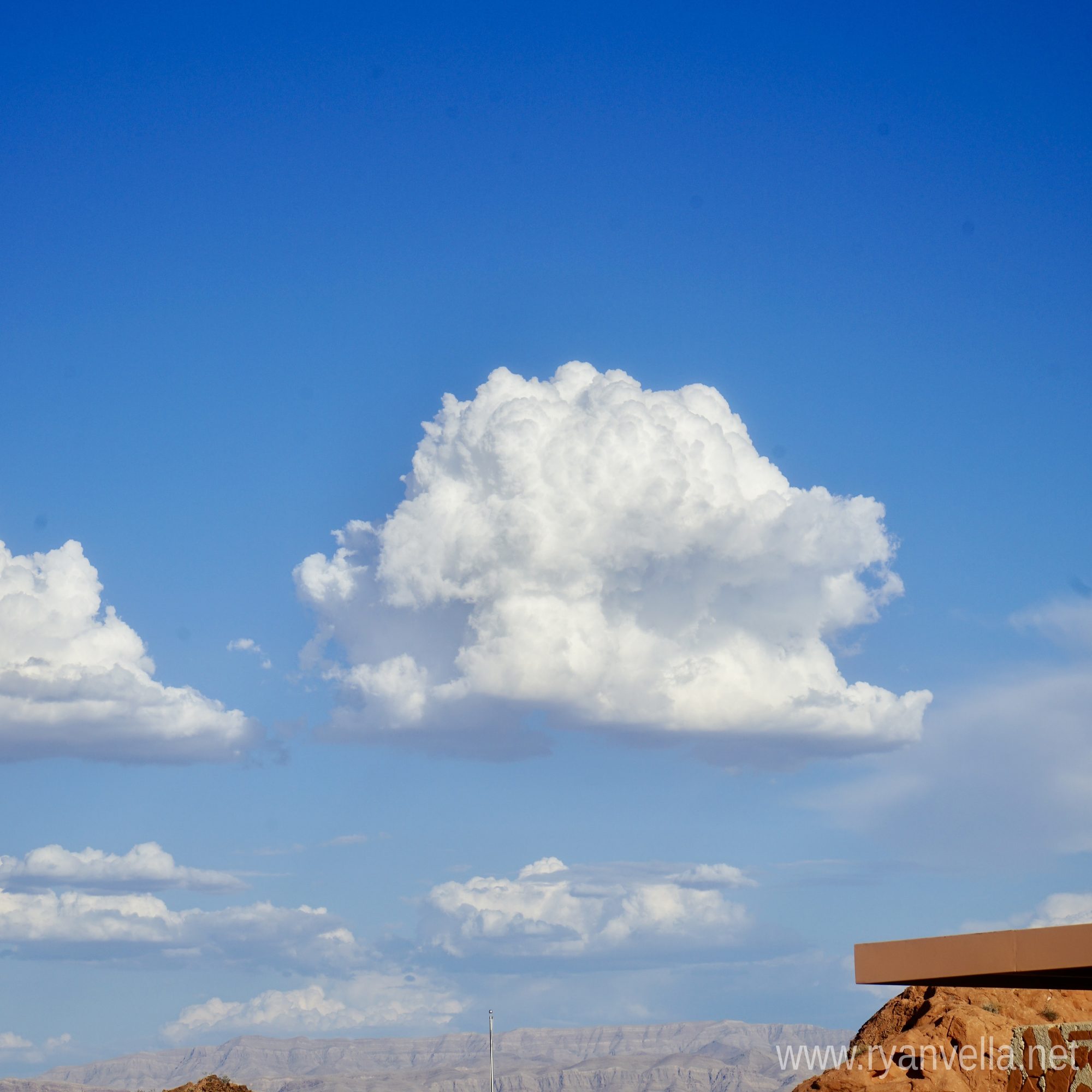 A tall cumulus cloud building over a desert plateau, with red rock and distant mesas below